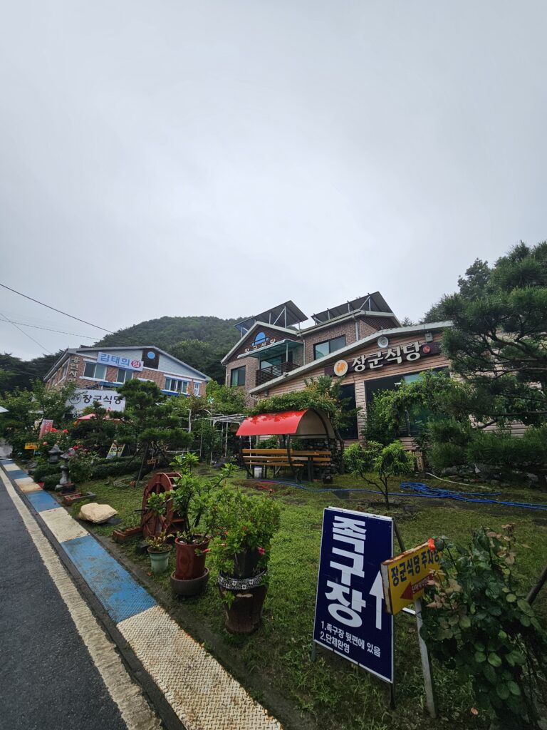 Garden-front view of Janggun Sikdang with trees, bench, decorative windmill, and jokgu direction sign.