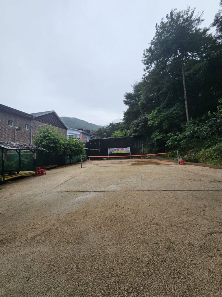Large outdoor jokgu court at Janggun Sikdang with orange net and forest around it.