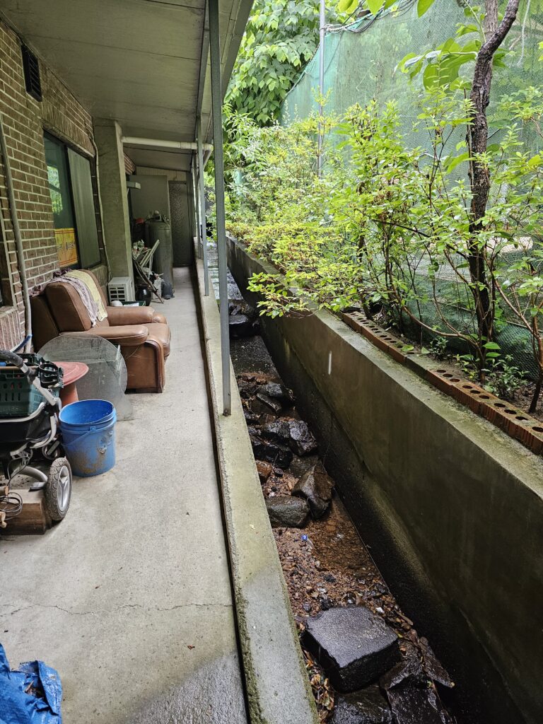 Concrete water channel behind Janggun Sikdang with rocks and little standing water.