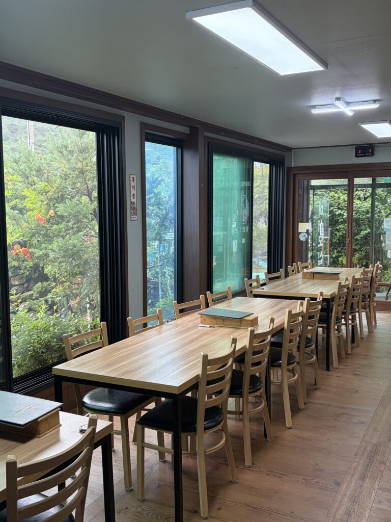 Window-side dining tables overlooking wet summer greenery at Janggun Sikdang.
