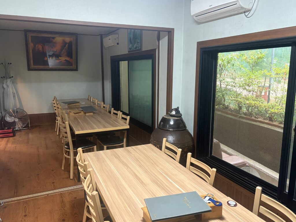 Dining tables, large jar, and window facing greenery near the jokgu court area.