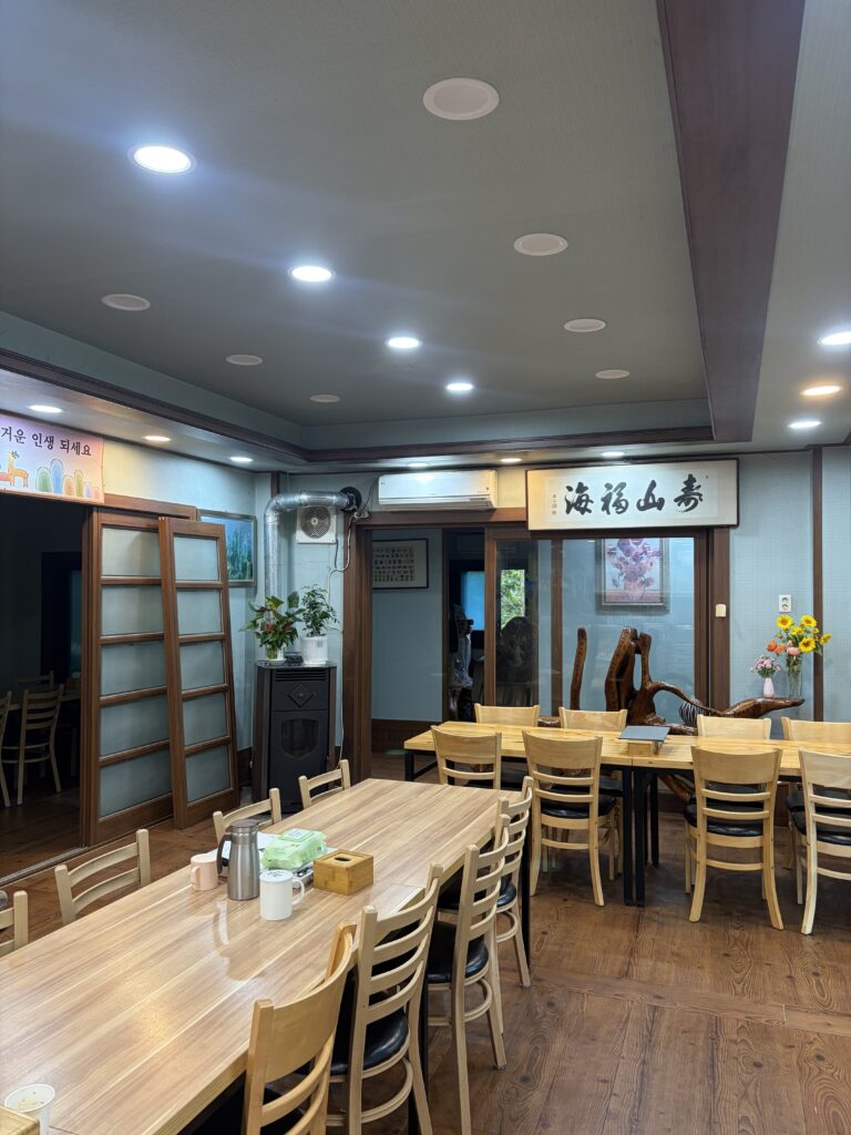 Janggun Sikdang main dining hall with wooden furniture, calligraphy, flowers, and wood sculpture.