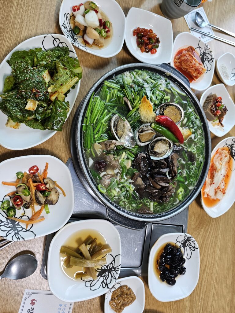 Large pot of duck baeksuk with abalone, mushrooms, chives, green onion, and red and green chilies.