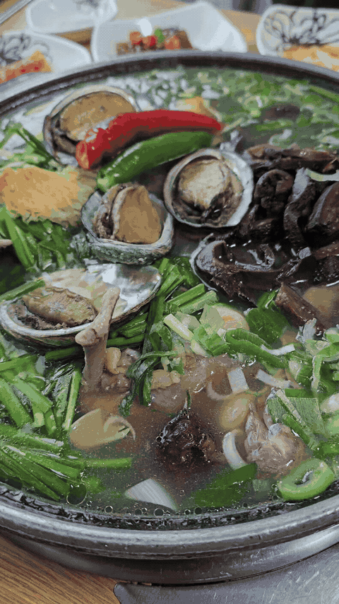 Boiling duck baeksuk pot with steam, bubbles, vegetables, meat, and abalone.