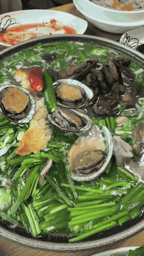Close moving view of abalone, chives, mushrooms, and chilies in duck baeksuk.