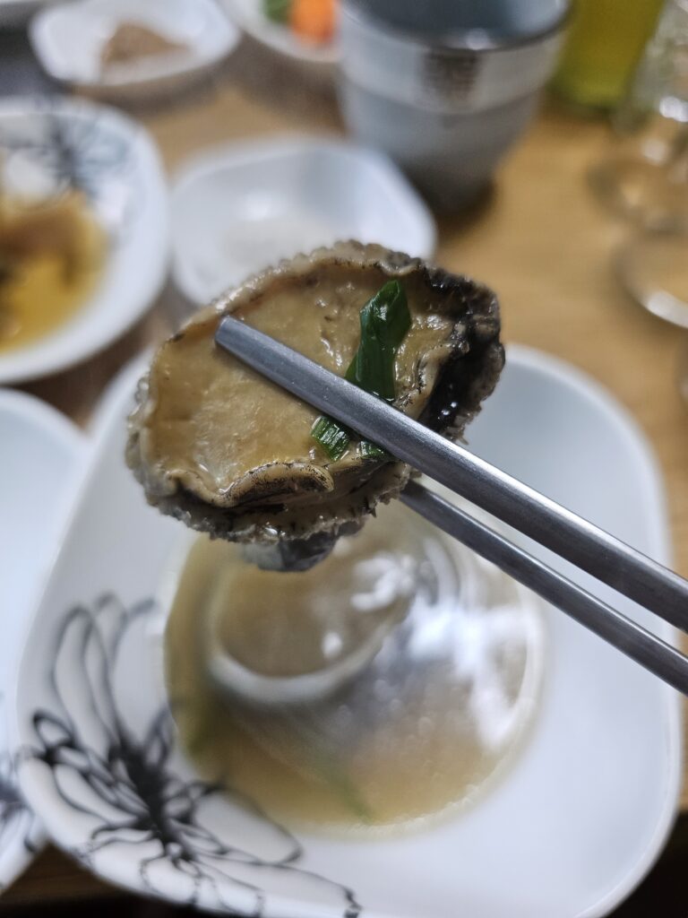 Close-up of cooked abalone meat with green onion held in chopsticks.