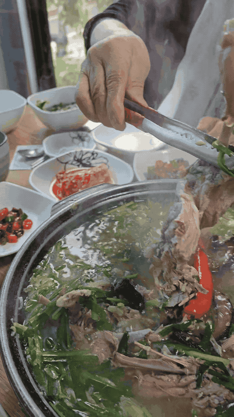 Large duck leg portion lifted from neungi duck baeksuk with metal tongs.