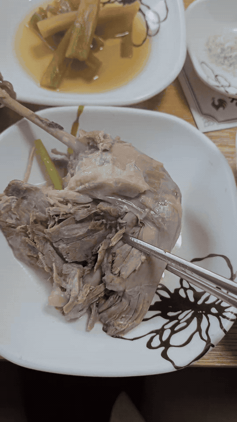Duck meat being pulled apart with chopsticks on a white plate.