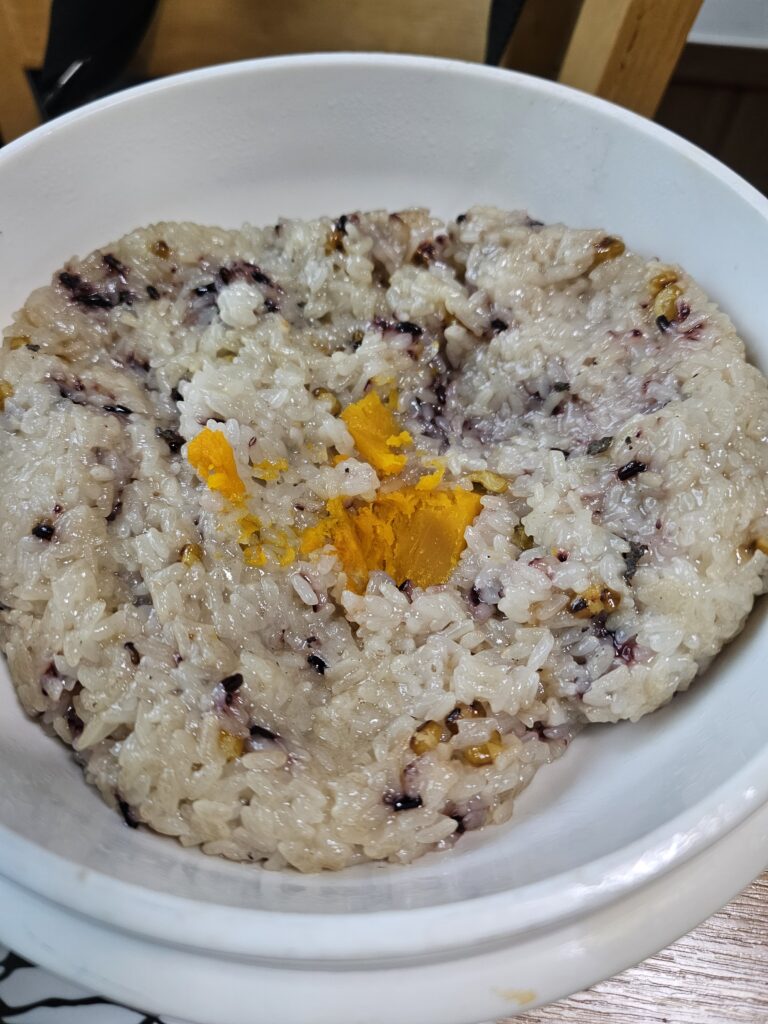 Glossy sticky multigrain rice with dark grains and a yellow-orange center ingredient.