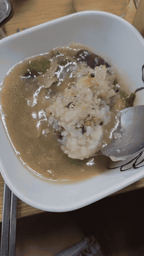 Sticky rice being loosened with duck broth, mushrooms, and green onion in a white bowl.