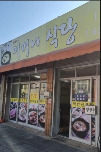 Entrance of Eomeoni Sikdang in Daejeon with a yellow sign, orange awning, and food photos near the door