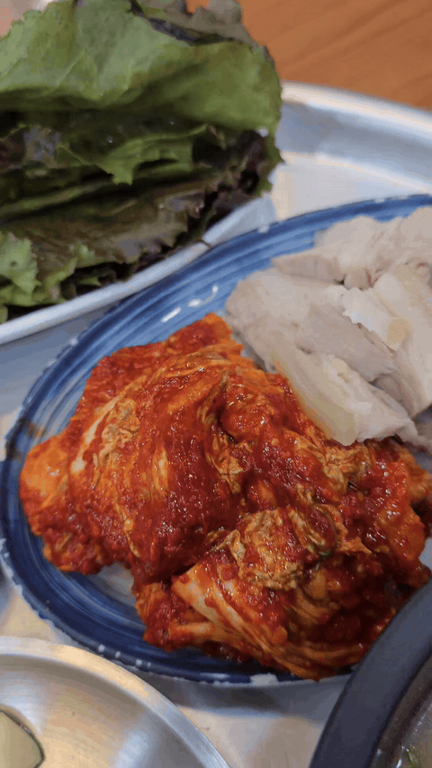 Bossam kimchi with red seasoning beside pork and vegetables