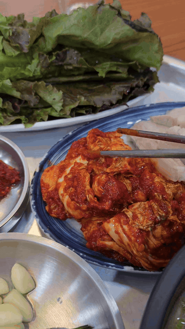 Bossam kimchi lifted with pork and vegetables nearby