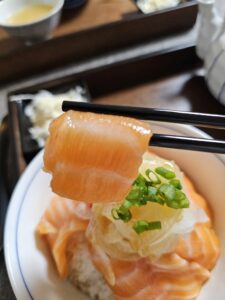 Chopsticks lifting a glistening salmon slice above the rice