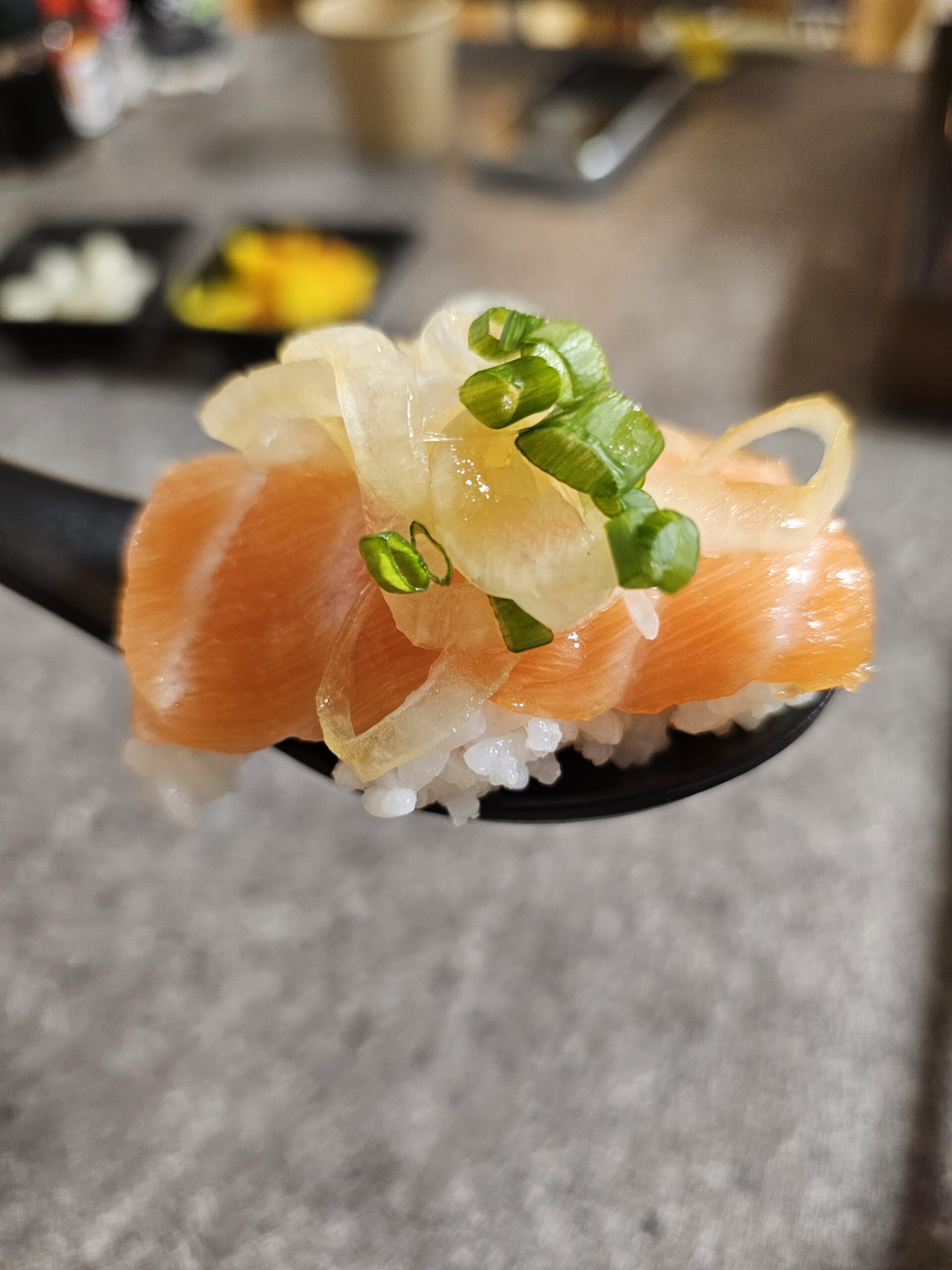 サーモン、薄切り玉ねぎ、ねぎをのせたひとさじのご飯