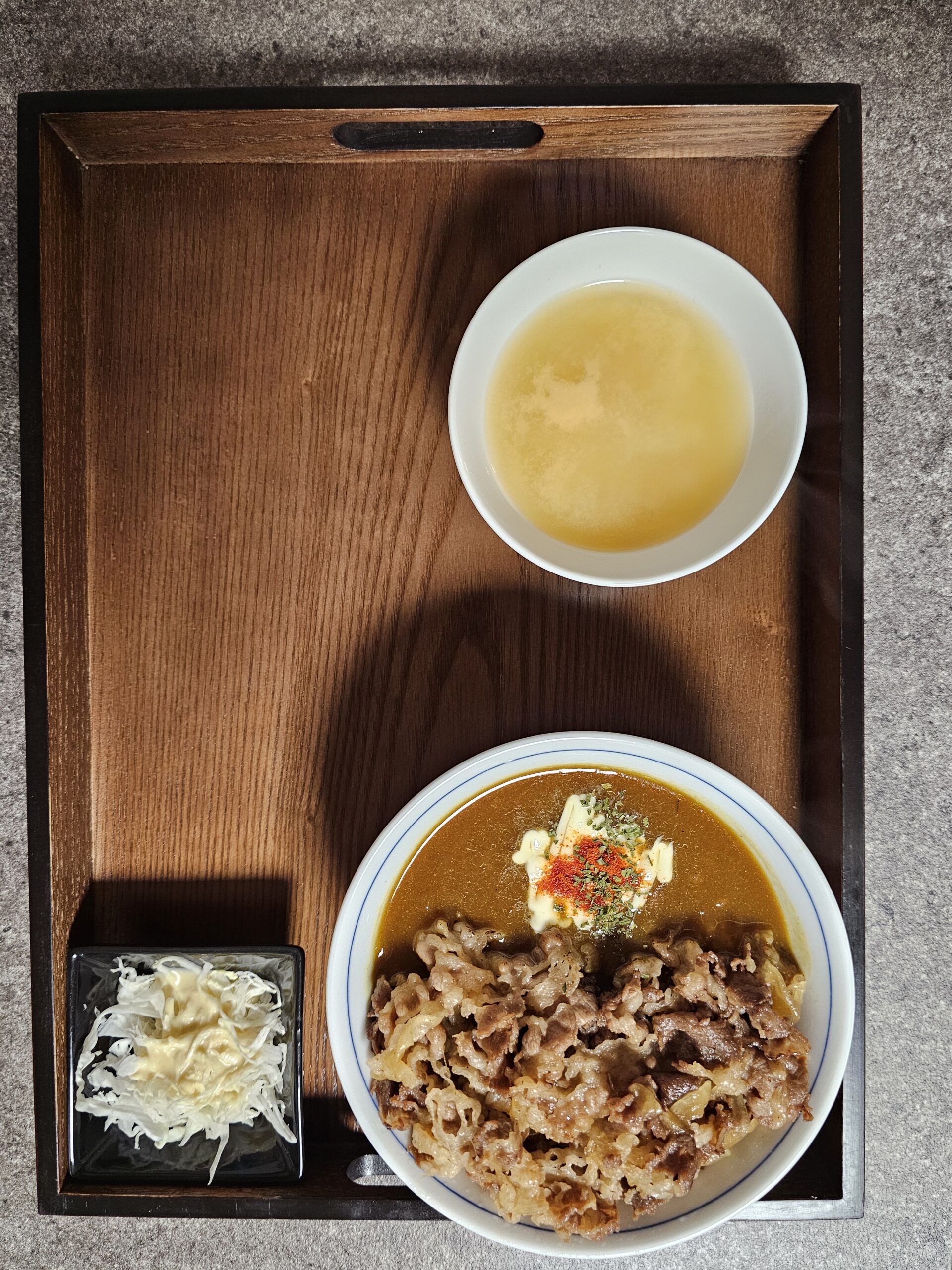 味噌汁とキャベツの横に置かれた、牛肉とマヨネーズがのったカレー牛丼