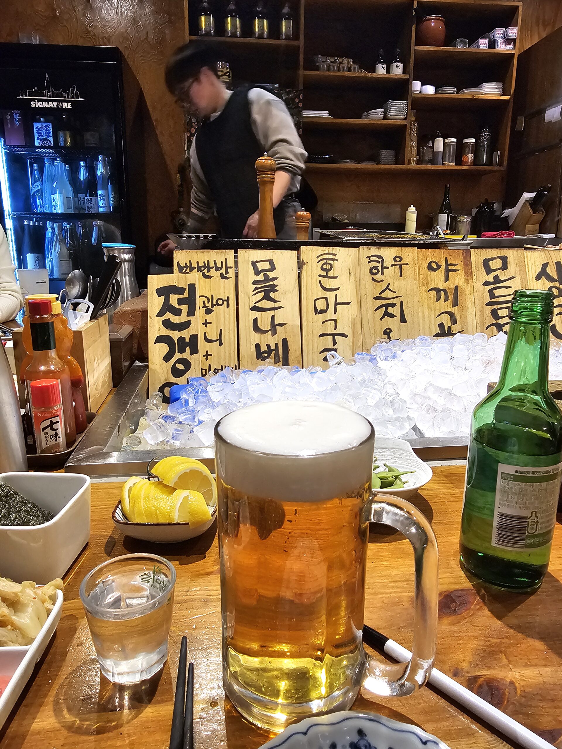 木製のメニュー板の下にあるカウンターの焼酎と生ビール