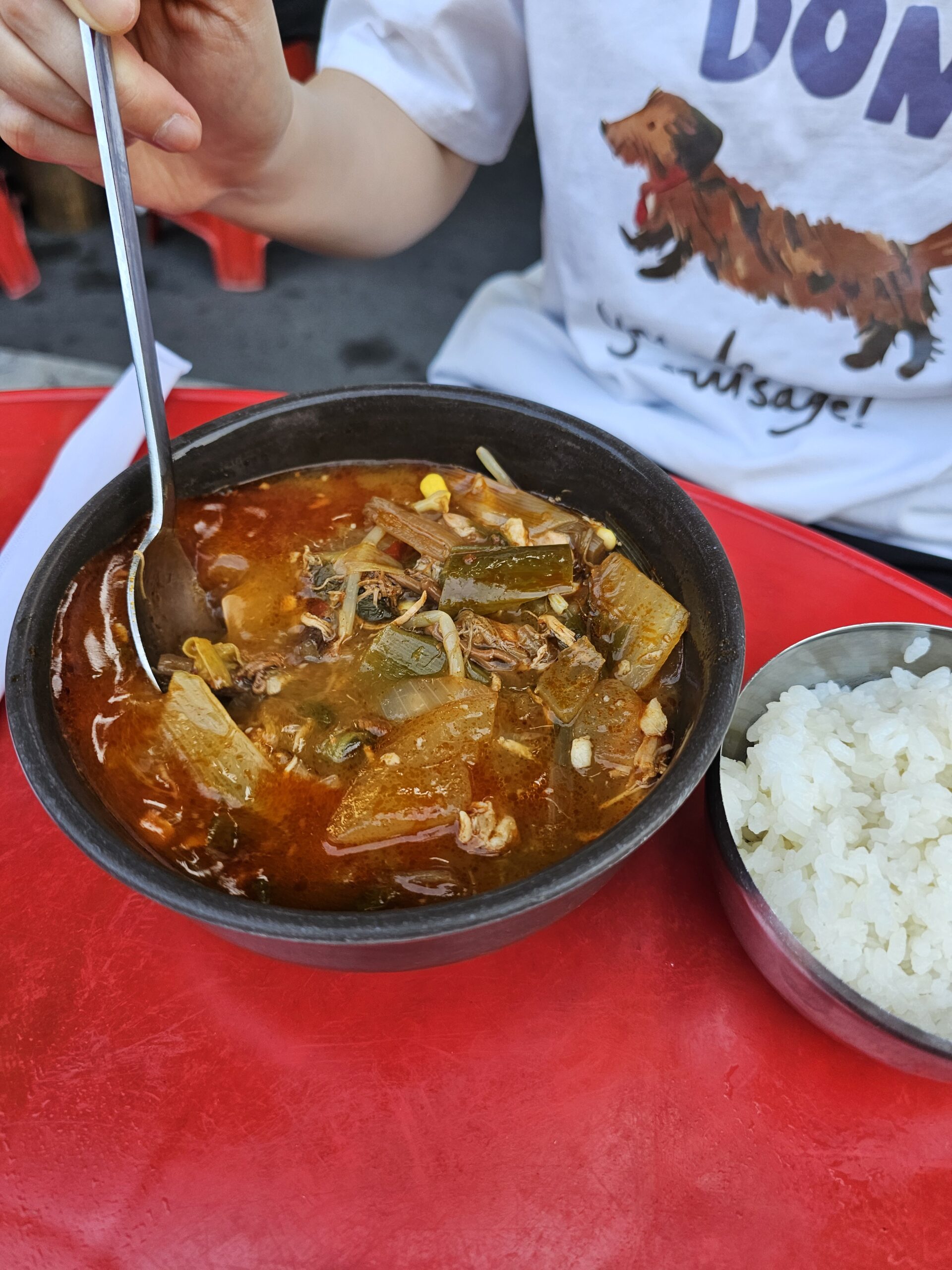 Deep red dakgaejang broth stirred to show bean sprouts