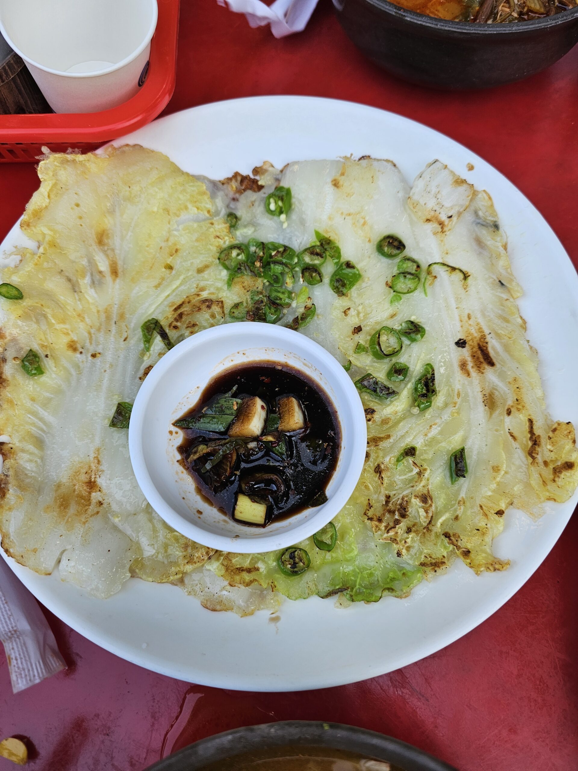 Golden Napa cabbage pancake topped with sliced green chili, with soy dipping sauce in the center