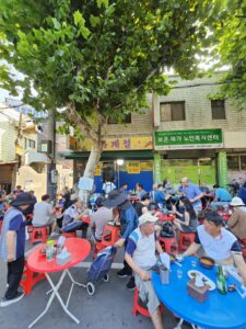 Restaurant front with chueotang and dakgaejang signs and red and blue tables under shady trees