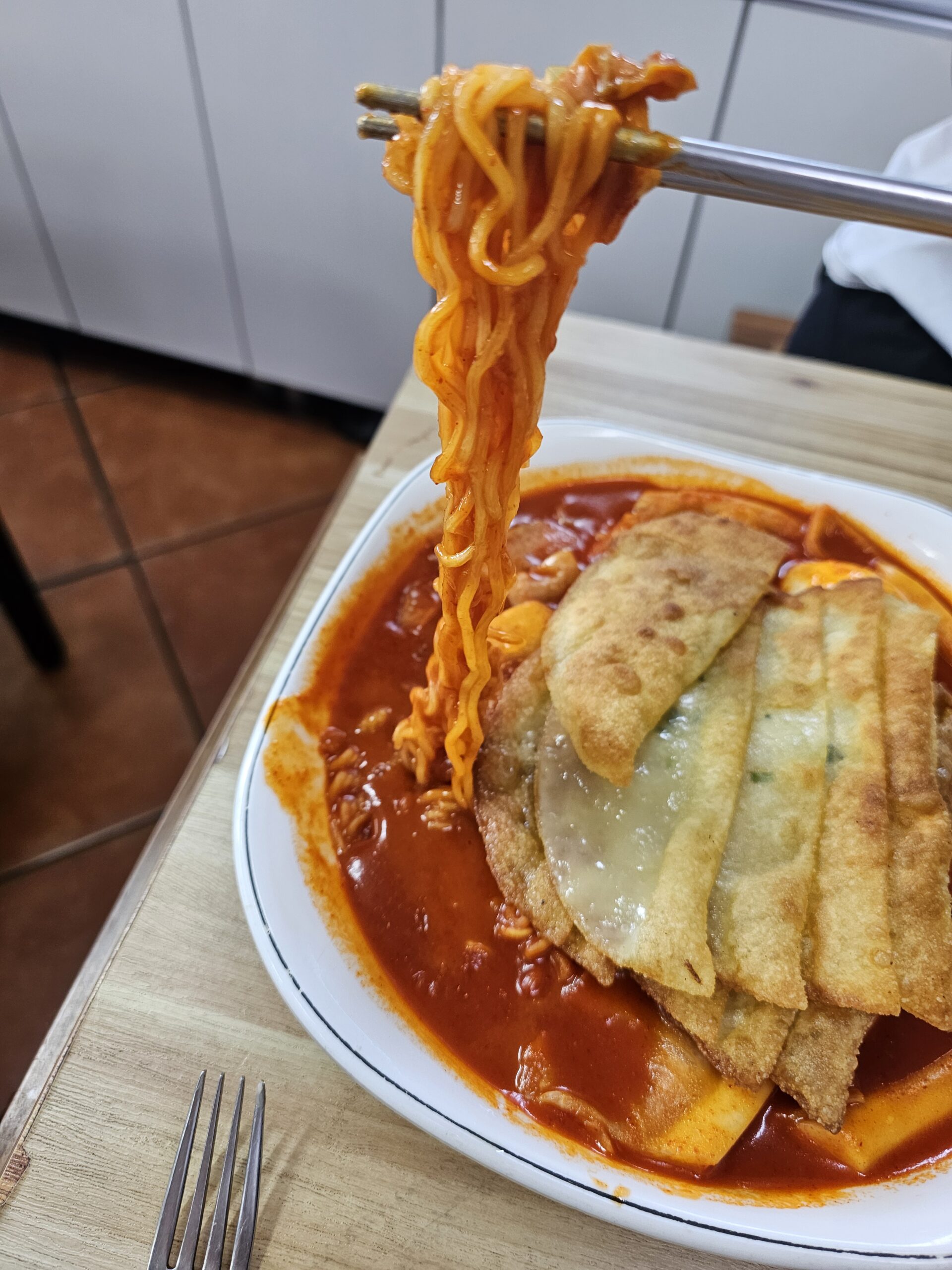 餃子ののった皿の上で、箸で持ち上げた赤いトッポッキソースのラーメンの麺