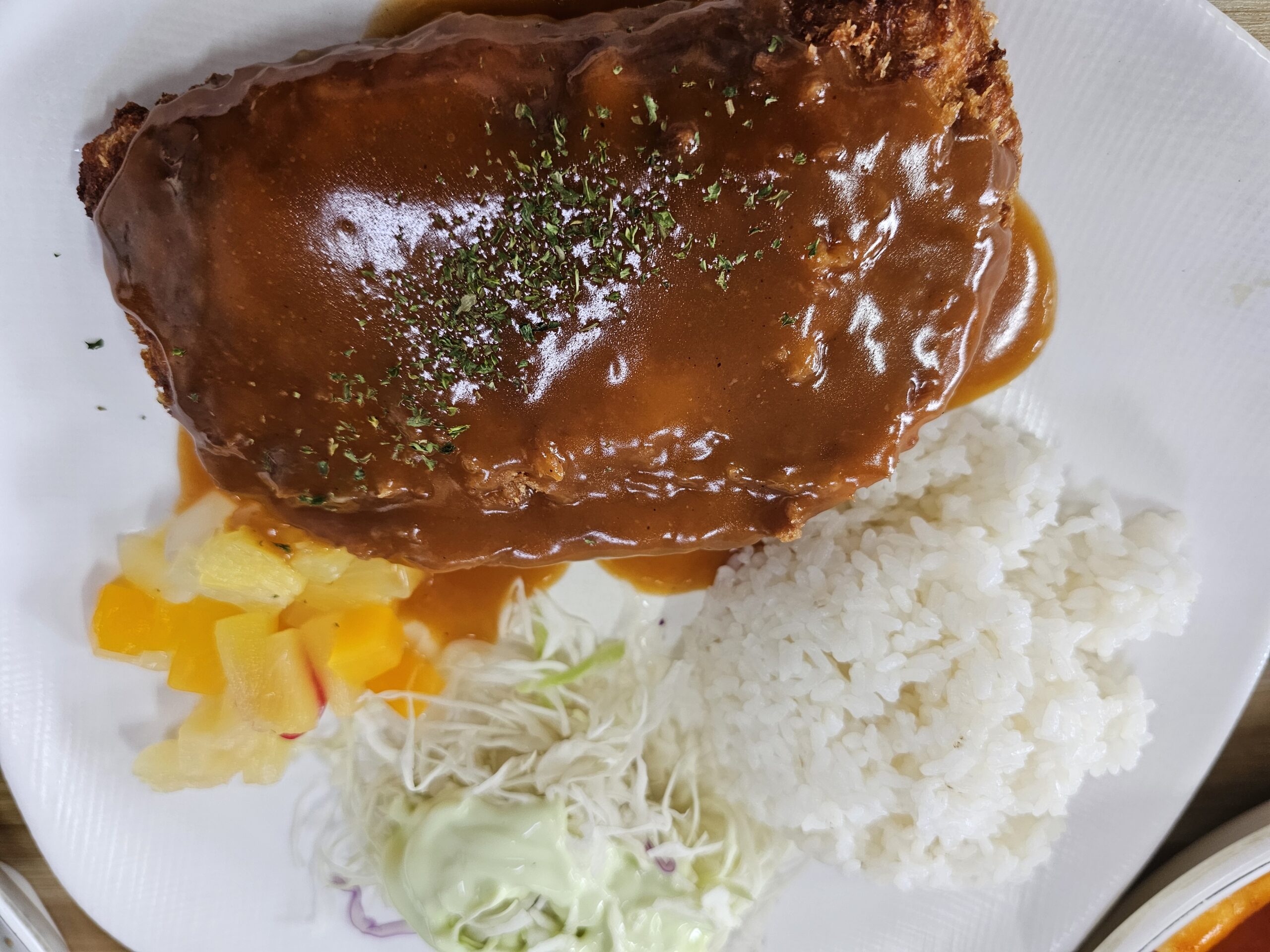 ソースがかかったチーズトンカツと白いご飯、キャベツサラダ、たくあん