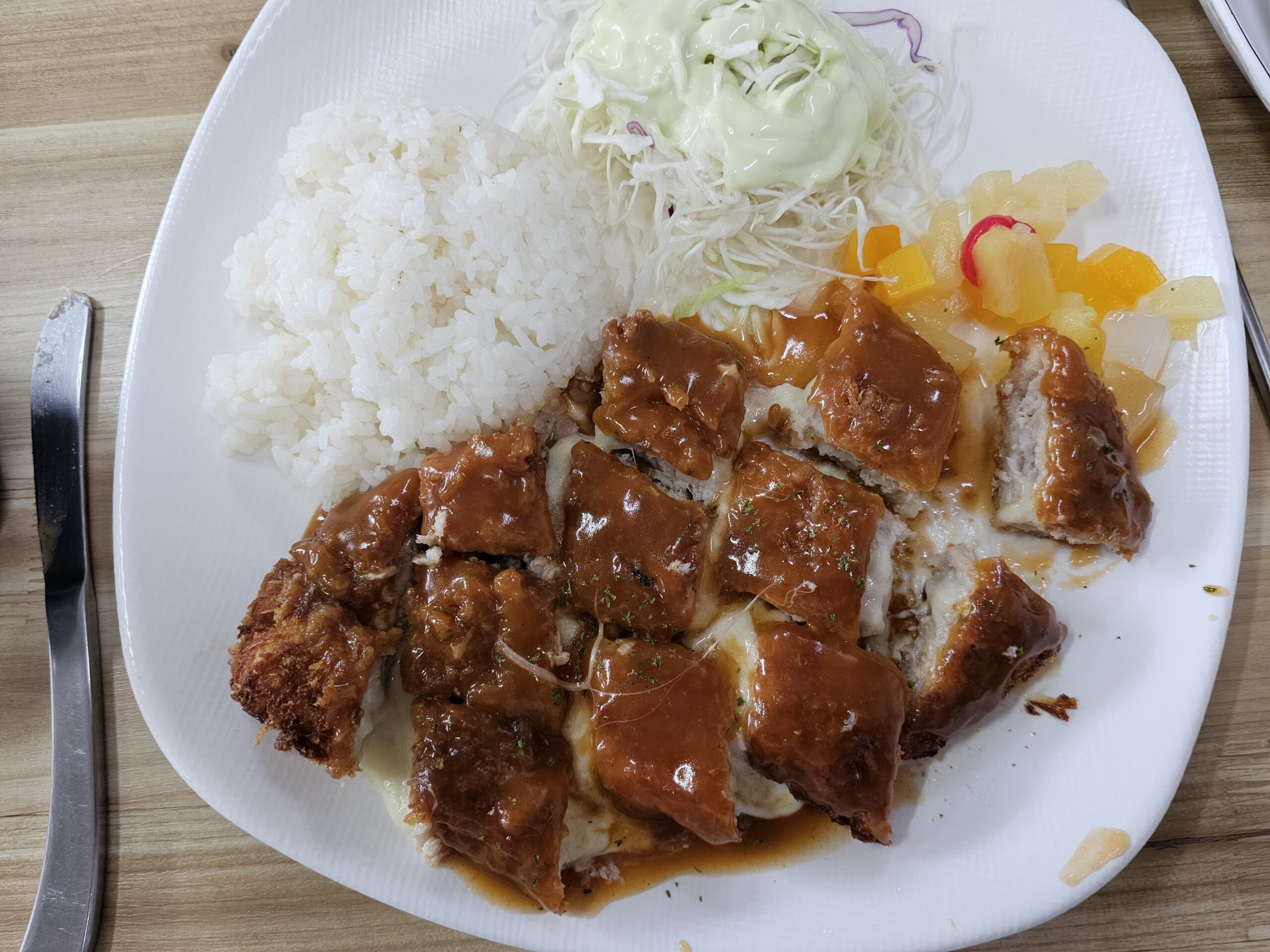 中にチーズが入った切り分けたチーズトンカツ、トンカツソース、ご飯、キャベツサラダ、たくあん