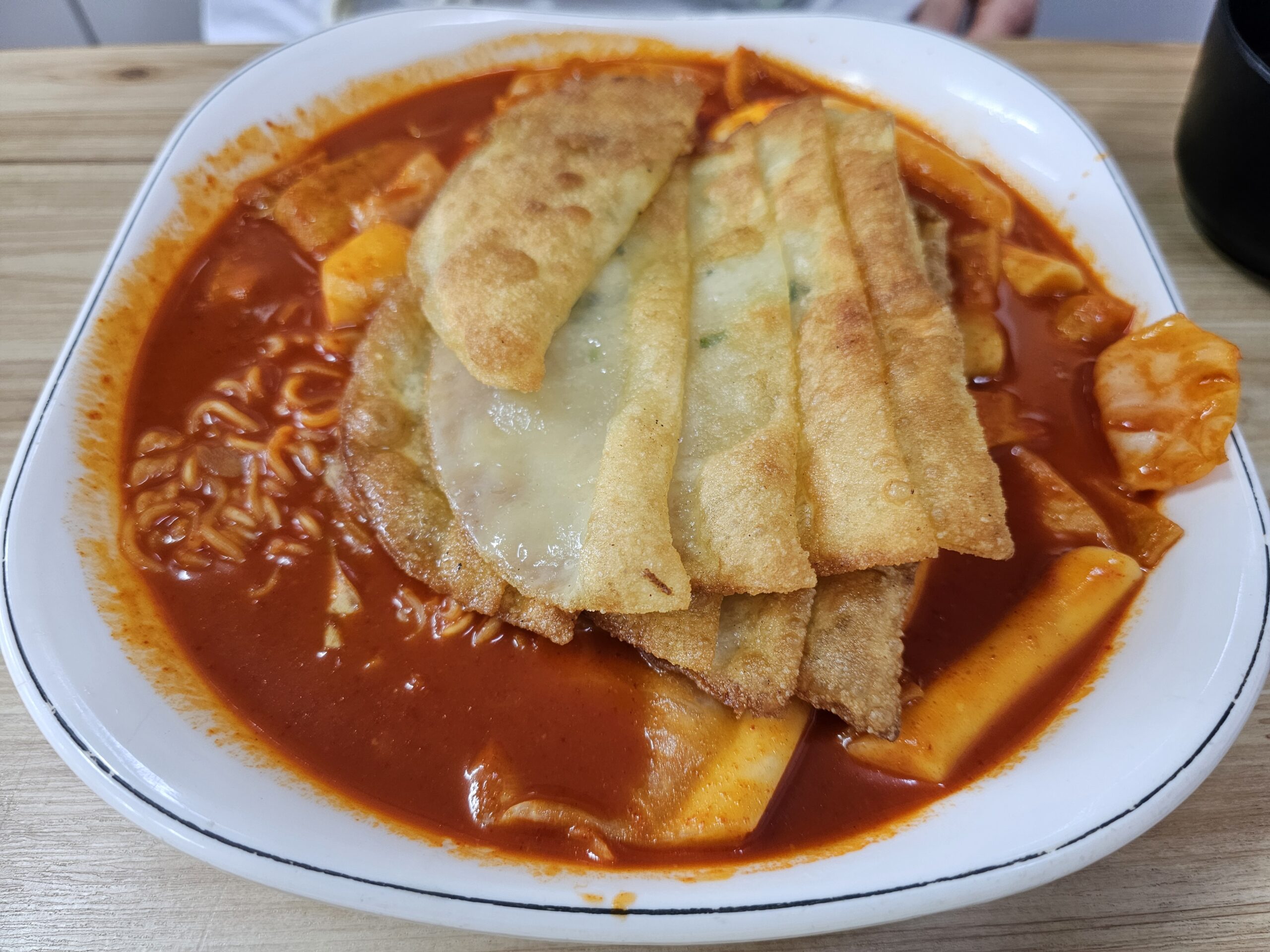 平たい餃子を数枚とラーメンの麺をのせた、赤いソースのスペシャルトッポッキ