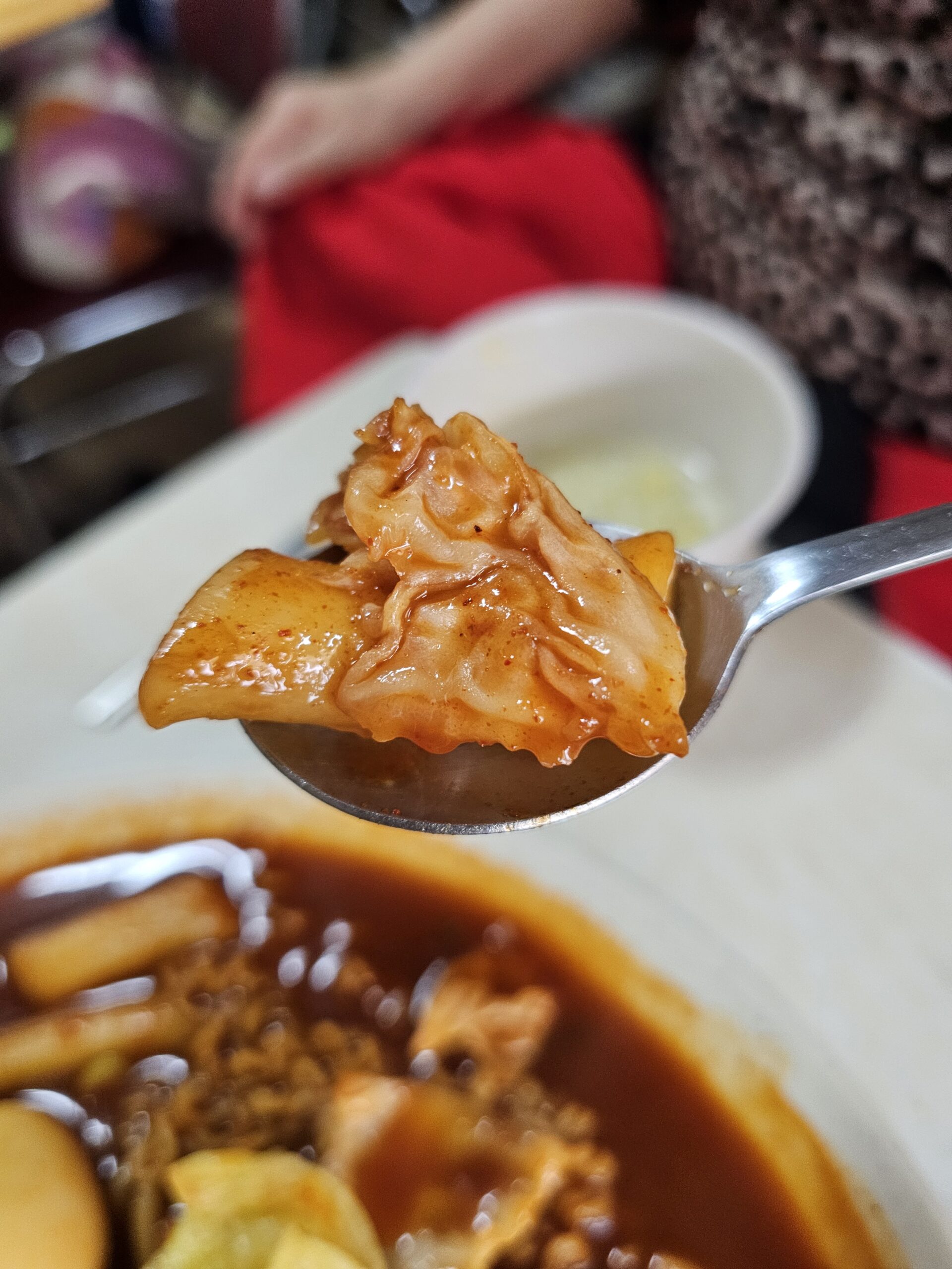 Rice cake and cabbage on a spoon with glossy chili-speckled sauce