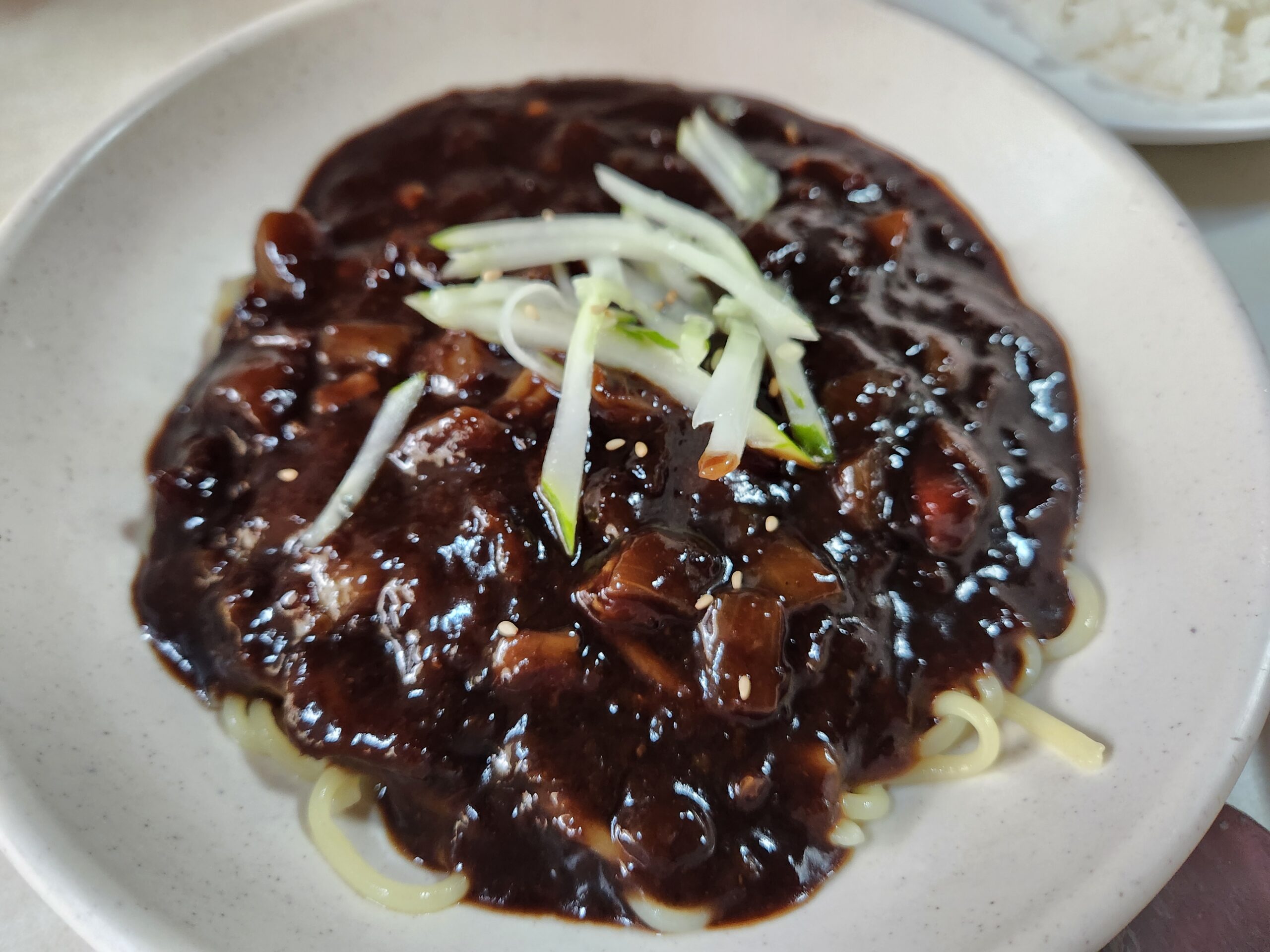 Glossy Jajangmyeon sauce covering noodles beneath cucumber strips